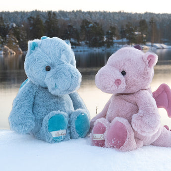 Two Lovely Dragos, Sapphire and Ruby, sit on a mound of snow in front of a wintry lake.